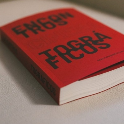 Livro vermelho com texto preto TOOGRÁFICOS sobre superfície branca