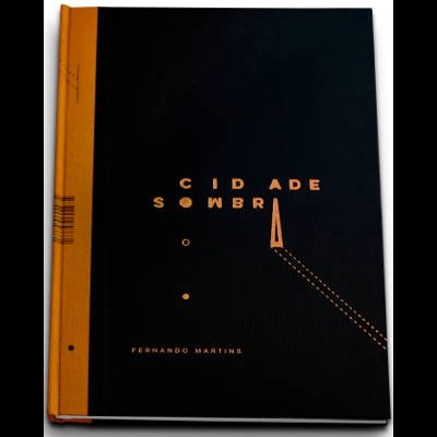 Livro preto com lombada laranja e título 'CIDADE SOMBRA' em letras douradas