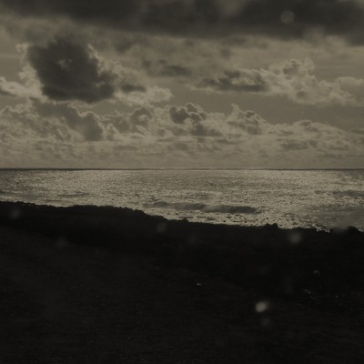 Paisagem costeira em preto e branco com nuvens escuras e texto inferior