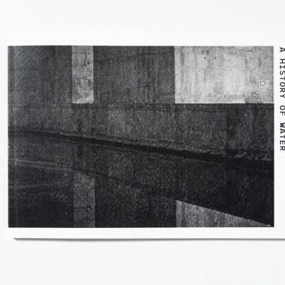 Livro com capa branca e fotografia em preto e cinza de superfície de água refletindo formas geométricas.