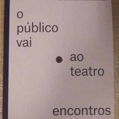 Livro cinzento claro com texto em preto sobre política e teatro numa superfície castanha
