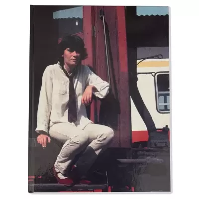 Mulher vestindo roupa branca sentada em estrutura metálica vermelha com vagão ao fundo