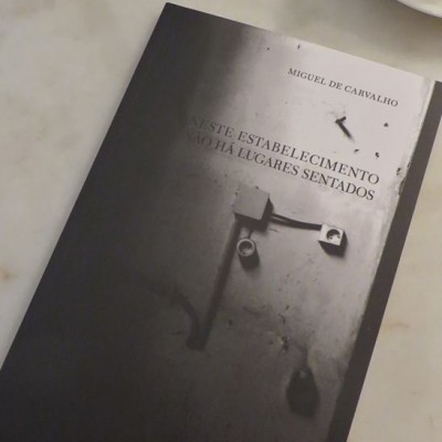 Livro de capa preta com título e imagem em tons de cinza, ao lado de uma chávena branca