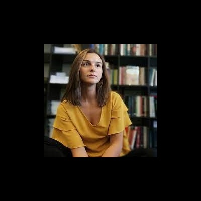 Mulher com vestido amarelo sentada em frente a estante de livros