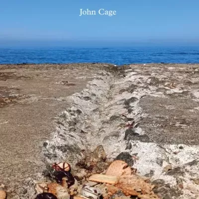 Costa rochosa com bolachas partidas e sumos, mar e céu azul com texto de John Cage.