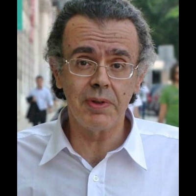 Homem de camisa branca e óculos ao ar livre, fundo urbano desfocado