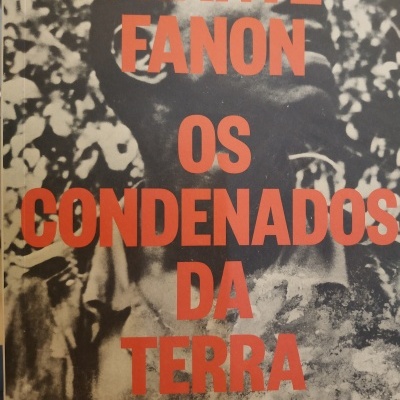 Capa de livro Os Condenados da Terra de Frantz Fanon com texto laranja sobre imagem em preto e branco