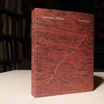 Livro vermelho com padrão e texto 'Caminhar oblíquo' e 'Duarte Belo' em mesa branca