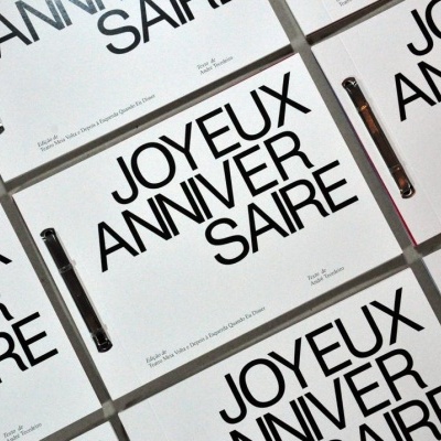 Caixas brancas com texto 'JOYEUX ANNIVERSAIRE' e canetas preto sobre superfície clara