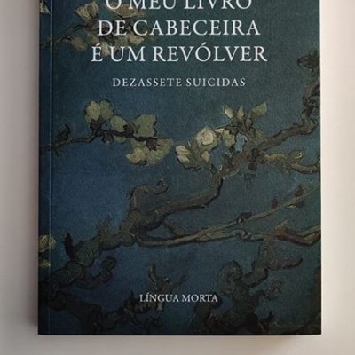 Livro 'O meu livro de cabeceira é um revólver' com capa azul escura e ilustração de ramos floridos