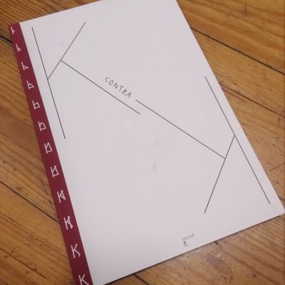 Livro branco com texto CONTRA e lombada bordô com letras K brancas