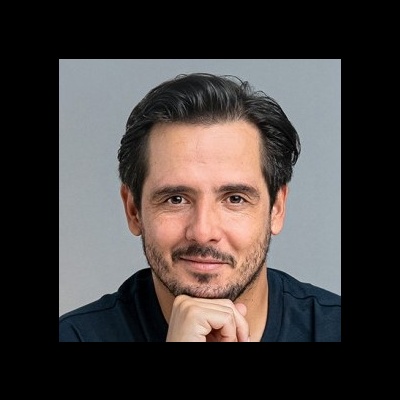 Homem adulto sorridente com barba curta e camisa preta, fundo cinza