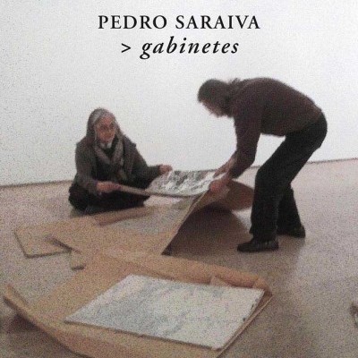 Duas pessoas manipulando grandes folhas em espaço com parede branca e texto