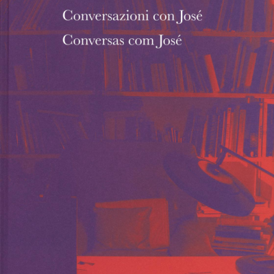 Capa do livro 'Conversazioni con José / Conversas com José' com estante de livros ao fundo e mesa com lâmpada e papéis.