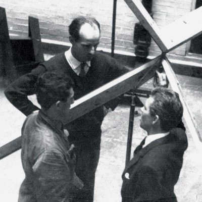 Três homens em ambiente industrial com estrutura metálica grande