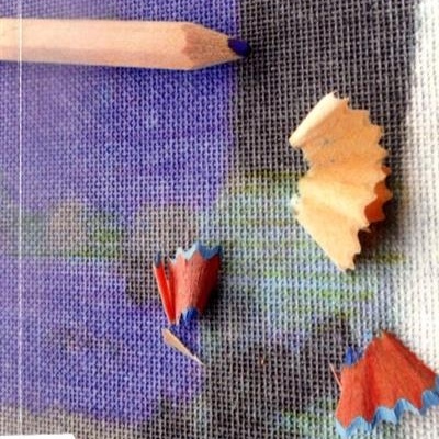 Livro com capa em textura têxtil azul e cinza, lápis azul e aparas de lápis coloridas