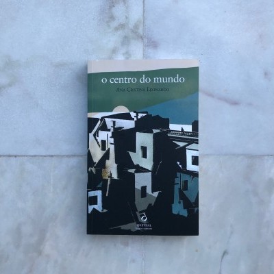 Livro 'o centro do mundo' com capa abstrata de edifícios em tons escuros sobre fundo claro