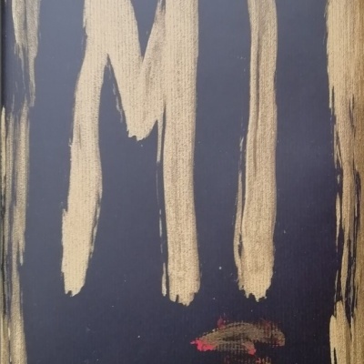Superfície negra pintada com letras douradas 'MI' e manchas vermelhas