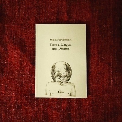 Livro 'Com a Língua nos Dentes' sobre tecido vermelho.