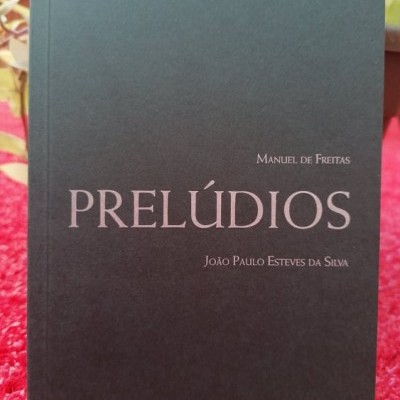 Livro preto com texto prateado PRELÚDIOS sobre tecido vermelho