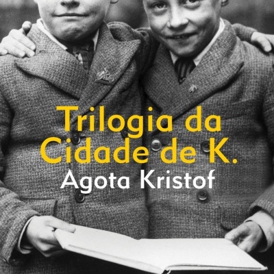 Capa do livro Trilogia da Cidade de K. com dois rapazes de casacos vintage e um livro