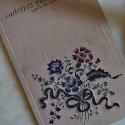 Capa de livro bege com flores e texto 'cadeiras vazias paulo da costa domingos'.