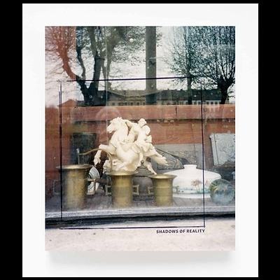 Estátua decorativa de cerâmica branca com três figuras num cavalo, sobre suportes dourados, numa vitrina com reflexos exteriores