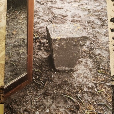 Bloco de pedra cinzenta sobre chão de terra ao lado de superfície refletora com moldura em madeira