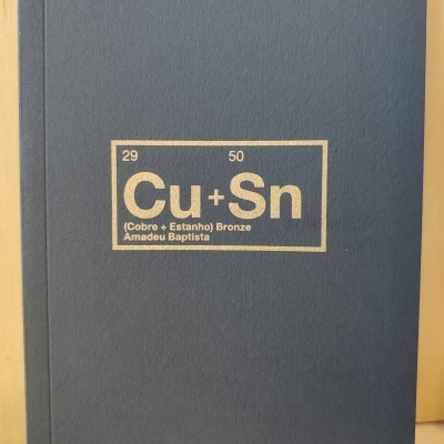 Capa azul escuro de livro com texto dourado Cu + Sn e outros detalhes