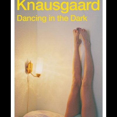Capa do livro Knausgaard Dancing in the Dark com imagem de pernas estendidas na parede e abajur aceso.