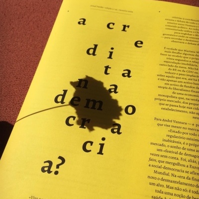 Página amarela de revista aberta com texto em português e sombra de folha