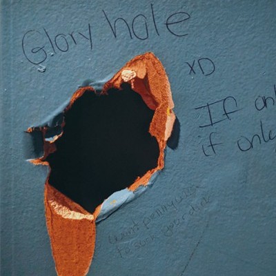 Buraco irregular numa parede azul com tinta descascada e inscrições escritas à volta.