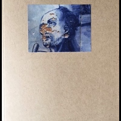 Caderno com capa cinza e imagem pequena de rosto humano azul com manchas laranja