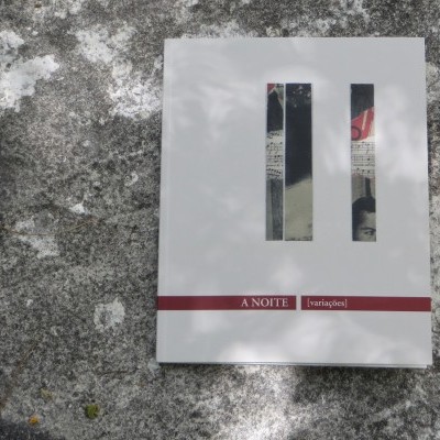 Pacote branco com duas janelas retangulares e texto 'A NOITE [solidões]' sobre pedra cinzenta