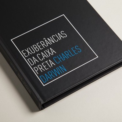 Livro preto com texto EXUBERÂNCIAS DA CAIXA PRETA CHARLES DARWIN na capa