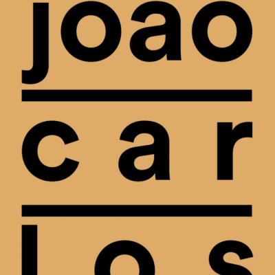 Texto joão car los escrito em preto sobre fundo castanho alaranjado