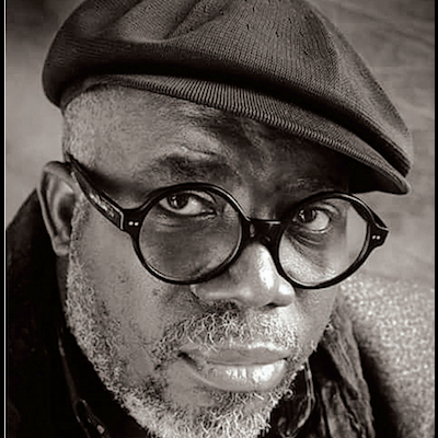 Homem com boina castanha e óculos pretos com fundo cinza