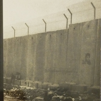 Capa do livro com imagem de muro alto de cimento com arame farpado e texto vermelho e preto