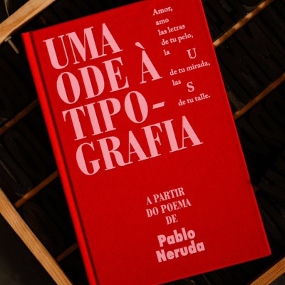 Livro vermelho com texto branco sobre tipografia e poema de Pablo Neruda numa superfície preta com moldura de madeira.