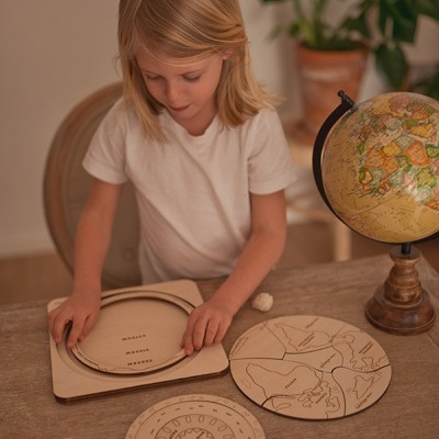 Criança a jogar com quebra-cabeças educativo de madeira ao lado de um globo terrestre