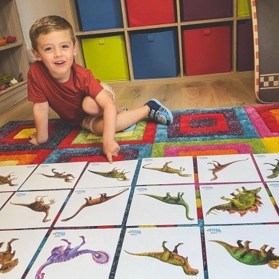 Menino sentado em tapete colorido com cartas de dinossauros espalhadas no chão