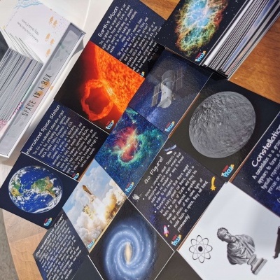 Cartões informativos sobre espaço com imagens da Terra, galáxias e ciência sobre mesa de madeira.