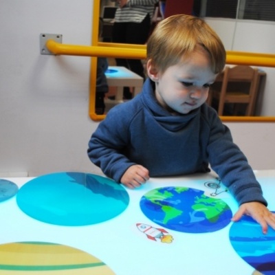 Criança com suéter azul interage com superfície iluminada e círculos coloridos