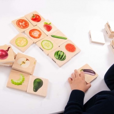 Peças de dominó de madeira com imagens de frutas e legumes e criança a jogar