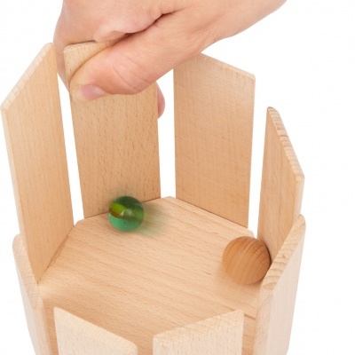 Dispositivo hexagonal de madeira clara com bolas e mão segurando peça