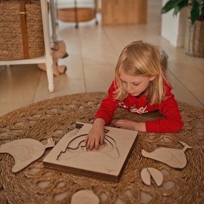 Criança a brincar com puzzle de madeira de peixe sobre tapete trançado