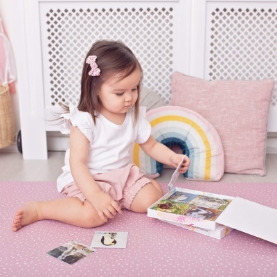 Criança brincando com cartas e caixa de jogo sentada em tapete rosa perto de almofadas coloridas