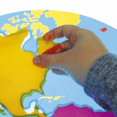 Mapa-múndi tipo puzzle com peças coloridas e mão a colocar peça amarela