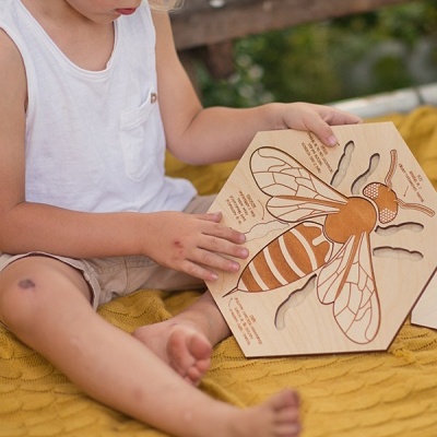 Criança segura puzzle de madeira com imagem de abelha em cobertor amarelo.
