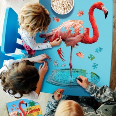 Crianças a montar puzzle de flamingo numa mesa azul com livro e taça de pipocas